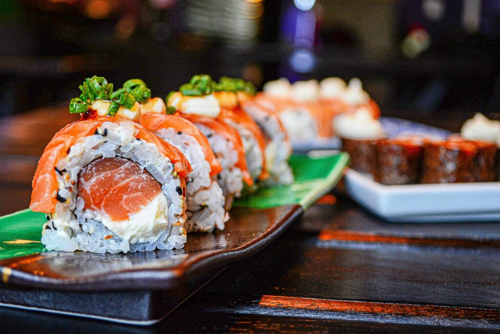 Sushi rolls topped with salmon and sauce on a wooden board