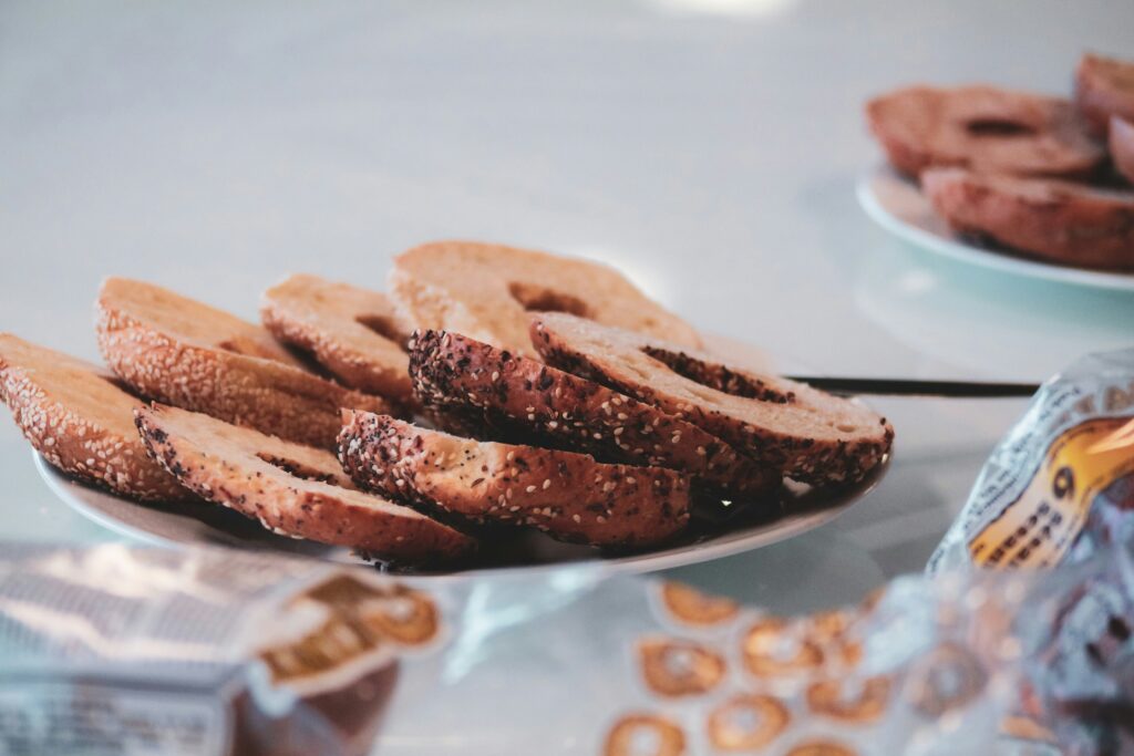 Plate of sliced bagels with assorted seeds, arranged on a table with packaged bread products in the background.