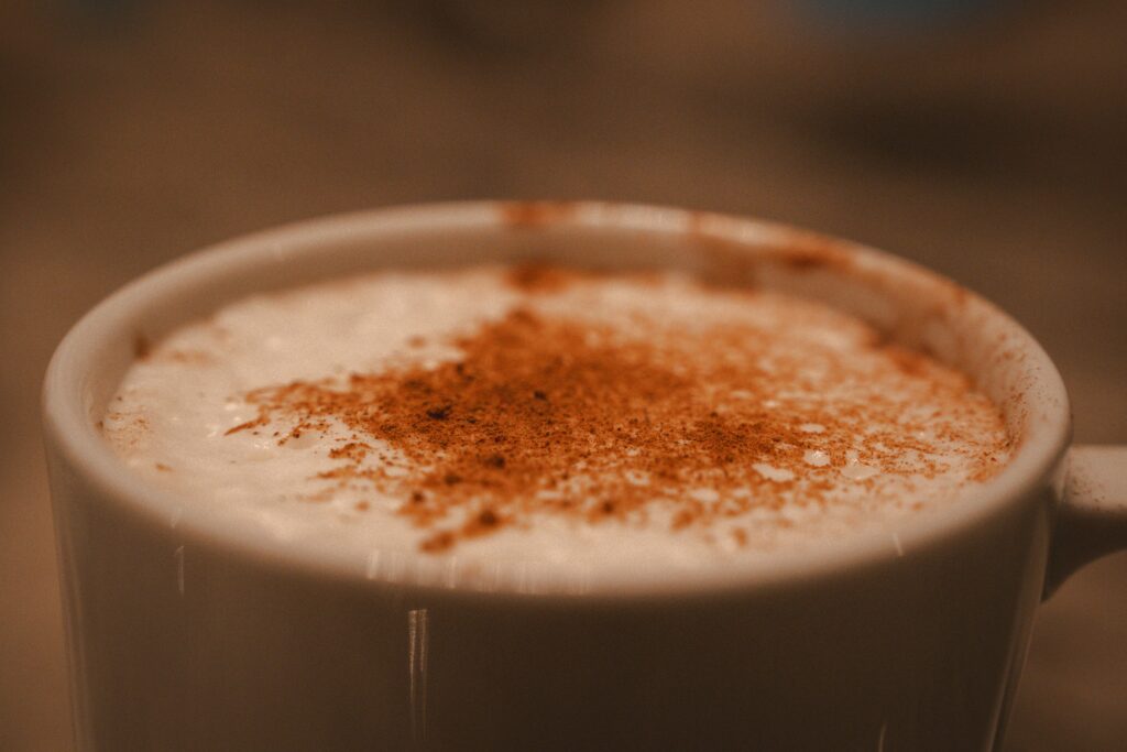 Close-up of a ceramic mug filled with a creamy hot beverage, topped with foam and a dusting of cinnamon.