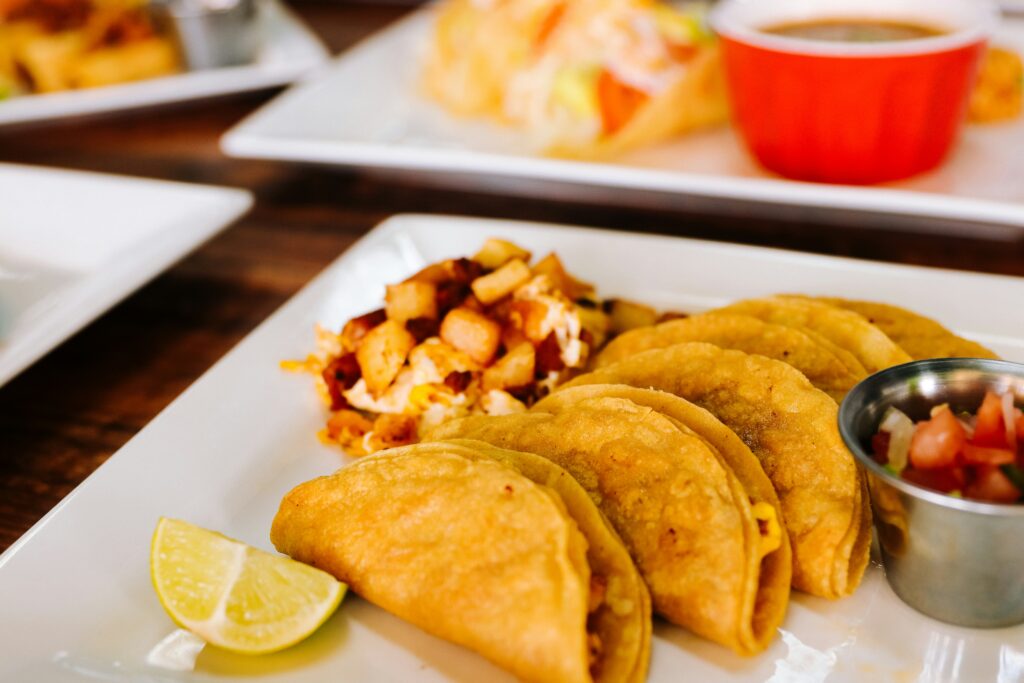 Plate of crispy tacos served with potatoes, salsa, and a lime wedge