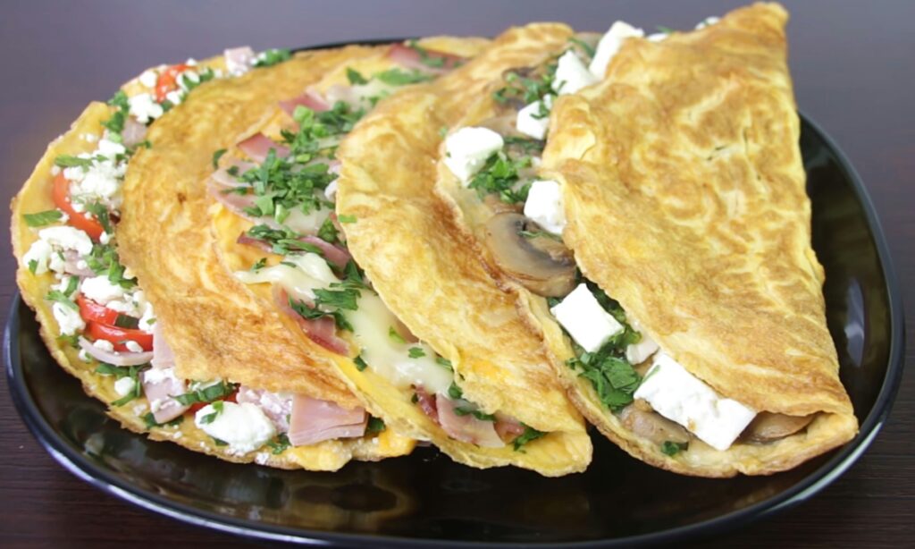 Folded omelets filled with cheese, herbs, and vegetables on a black plate